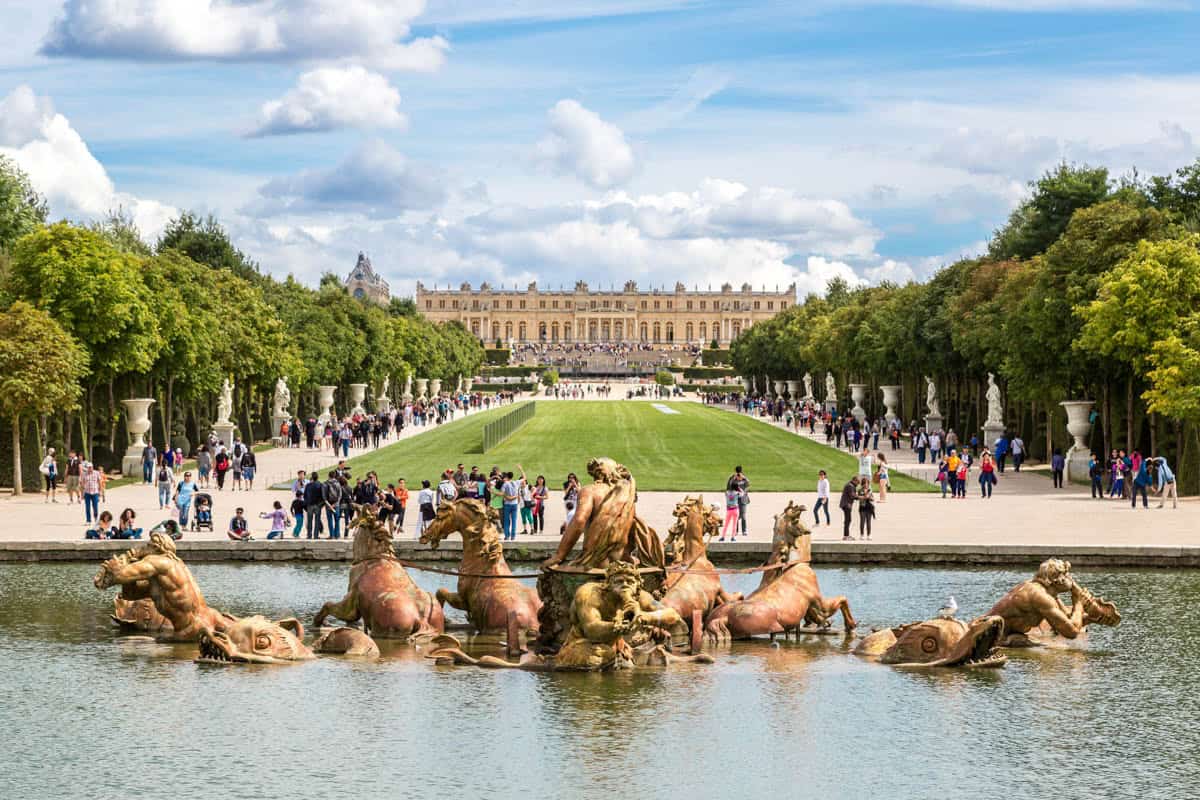 Latona Fountain sculptures and palace garden axis with visitors framed by palace and formal gardens at Palace of Versailles in Versailles, France.