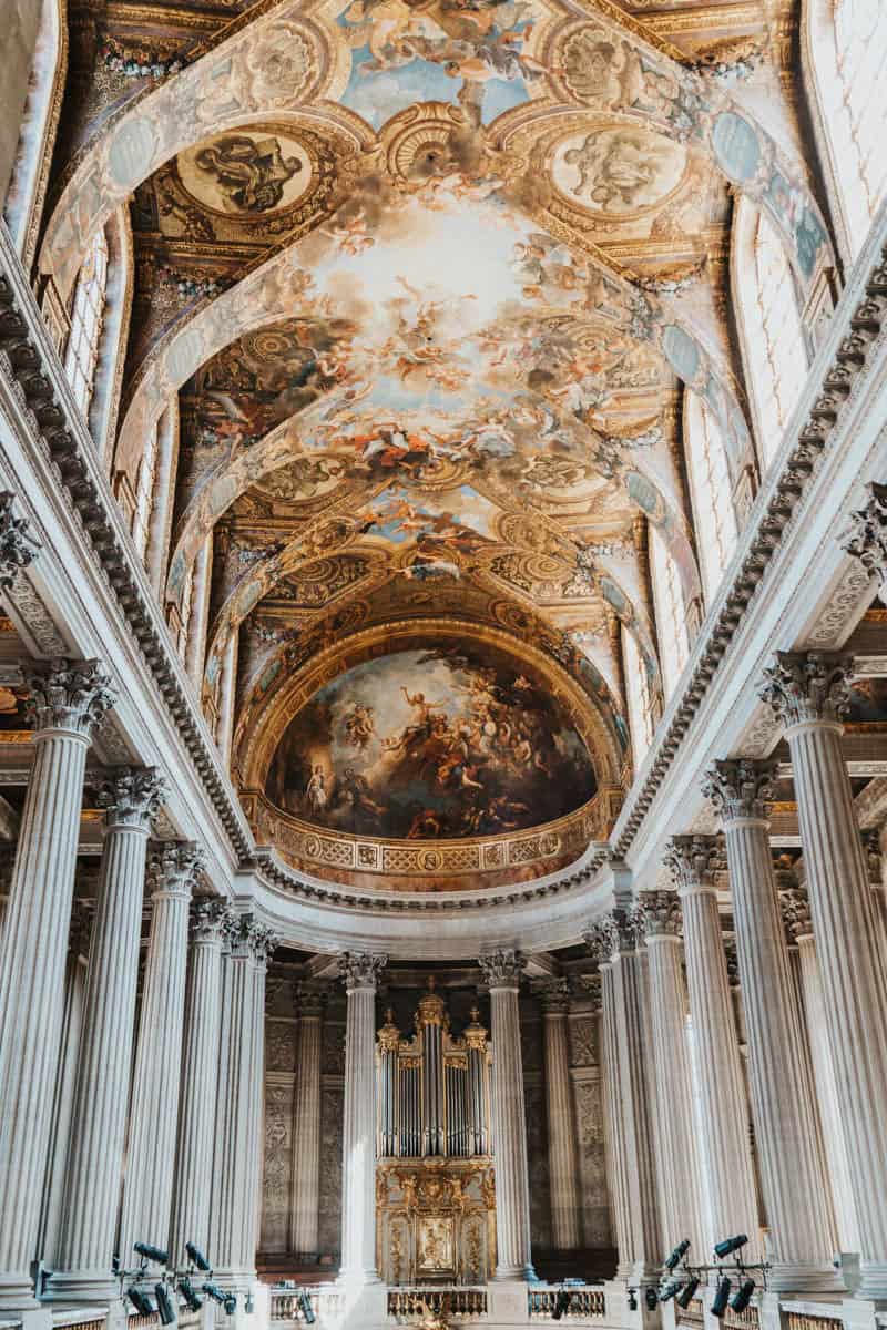 Palace of Versailles in Versailles, France pairs painted and gilded barrel-vaulted ceiling in an ornate gallery with palace details.