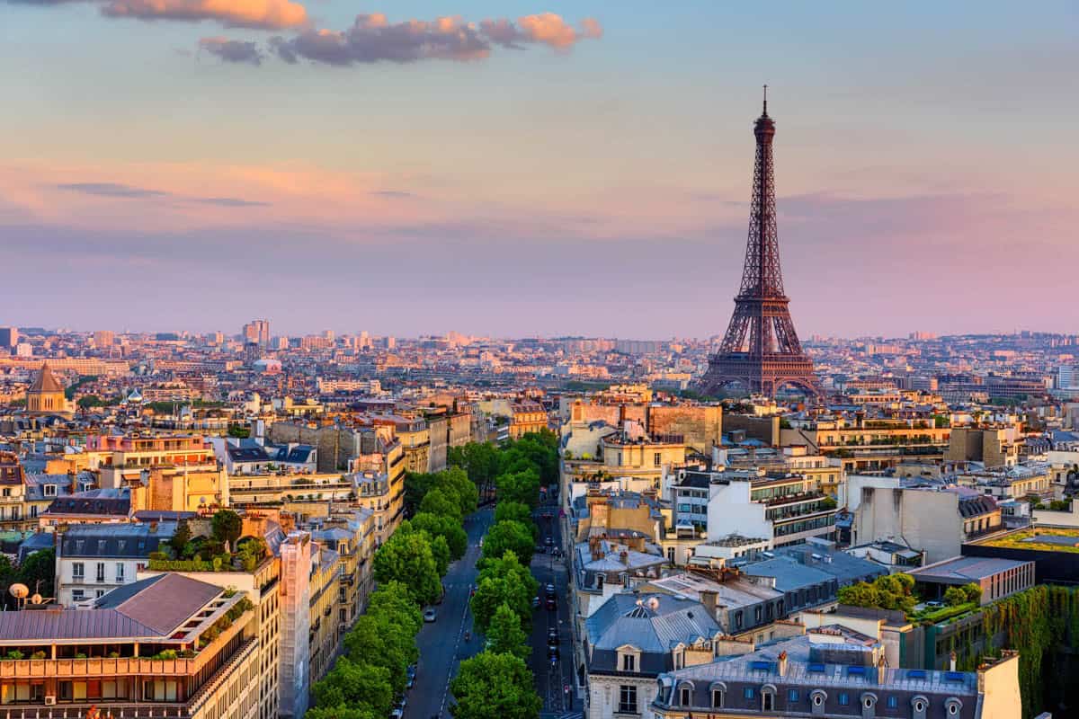 Eiffel Tower in Paris, France surrounds Eiffel Tower rising beyond Paris rooftops and a tree-lined avenue with tower and Paris monument.